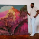 Oversized pink abstract artwork of mountain landscape leans up against white brick wall with man standing next to artwork