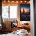 Oversized evergreen forest vertical wall art of sunset on the mountains hangs on wood paneled wall in rustic cabin.