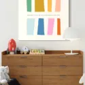 Huge colorful minimalist wall art featuring various sized rectangles with the quote "remember that you can start over at any time" hangs on white wall above changing table in modern nursery.