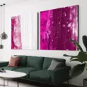 Set of two square abstract paintings in magenta hang side by side in living room above green couch.