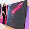 Extra large magenta wall art stacked against wall in modern neutral living room. Woman stands in front of art looking at top piece, in dark blue and magenta surreal style.