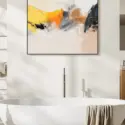 Square neutral abstract wall art in yellow, orange, and tan hangs above white soaking tub in modern bathroom.