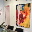 Large colorful abstract painting hangs by kitchen table in modern dinning room.