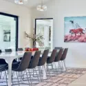 Surreal wall art of tiger with stripes being pulled off by a bird hangs on white wall in modern dinning room with long kitchen table.