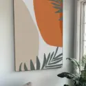 Extra large orange and tan abstract art with sage green tropical leaves hangs on white living room wall.