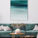 Contemporary living room features teal blue abstract artwork hanging on white wall above blue couch on white wall.