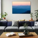 Large blue abstract wall decor of sunset over the mountains hangs on white wall in living room above navy blue couch.