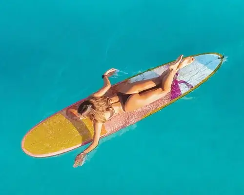 Photo of girl with yellow surfboard swimming out into the clear blue ocean.
