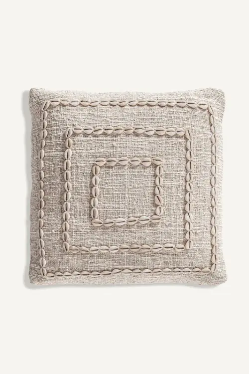 Seashell accent pillow in neutral tones on a white background.