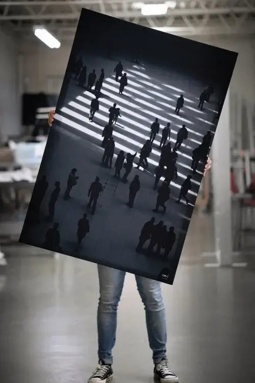 Massive black and white aerial photo of sidewalk in NYC is held by a person wearing jeans in a large warehouse.