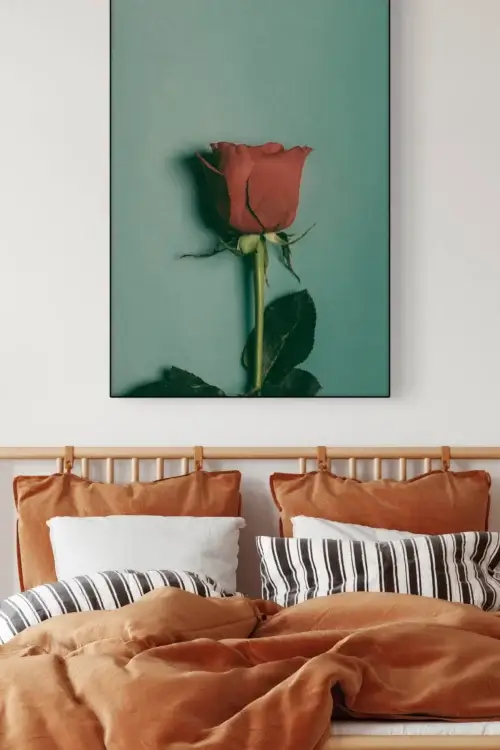 Massive minimalist flower wall art of photo of single red rose on teal blue background hangs above bed with orange duvet throw on messily.