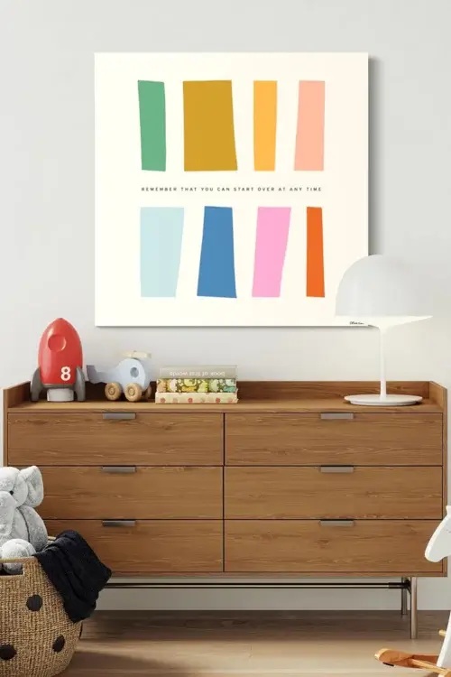 Huge colorful minimalist wall art featuring various sized rectangles with the quote "remember that you can start over at any time" hangs on white wall above changing table in modern nursery.