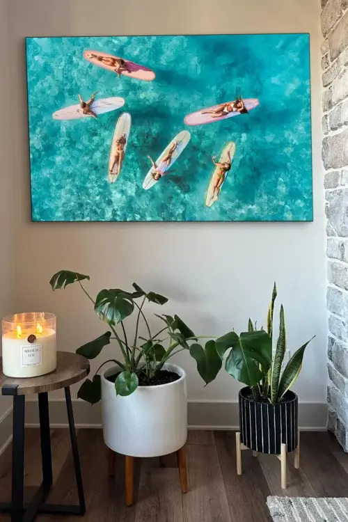 Aerial photo of surfer girls hanging on their boards in Hawaii hangs above indoor house plants and a big ass candle sitting on a side table in a living room