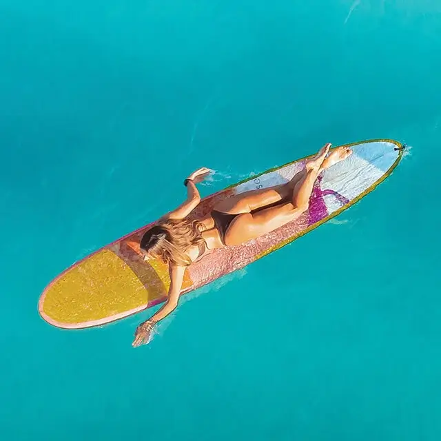Photo of girl with yellow surfboard swimming out into the clear blue ocean.