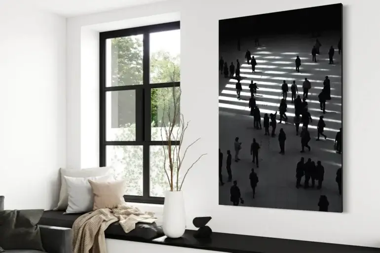 Huge black and white photography of people milling around on city street that is heavily shadowed hangs on white wall in minimalist black and white living room above black window seat bench.
