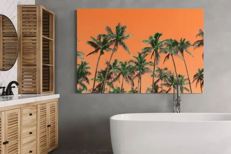Extra large colorful bathroom wall art with palm trees on orange background hangs on light grey wall above soaking tub in bathroom.