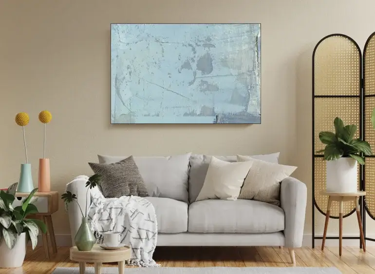 Large coastal abstract wall art in shades of light blue hangs above a couch in a modern beige living room