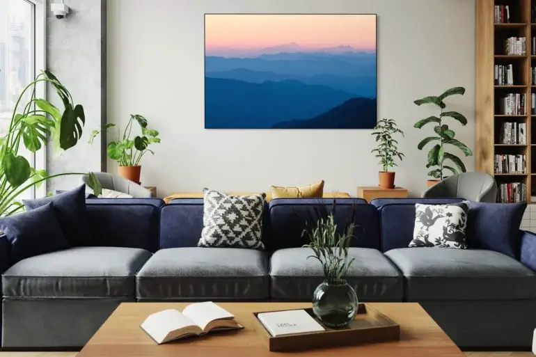 Large blue abstract wall decor of sunset over the mountains hangs on white wall in living room above navy blue couch.