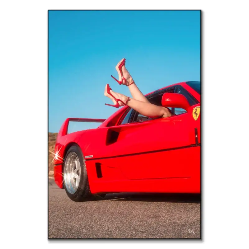 Red sports car with legs in red high heels playfully extending from the window under a blue sky.