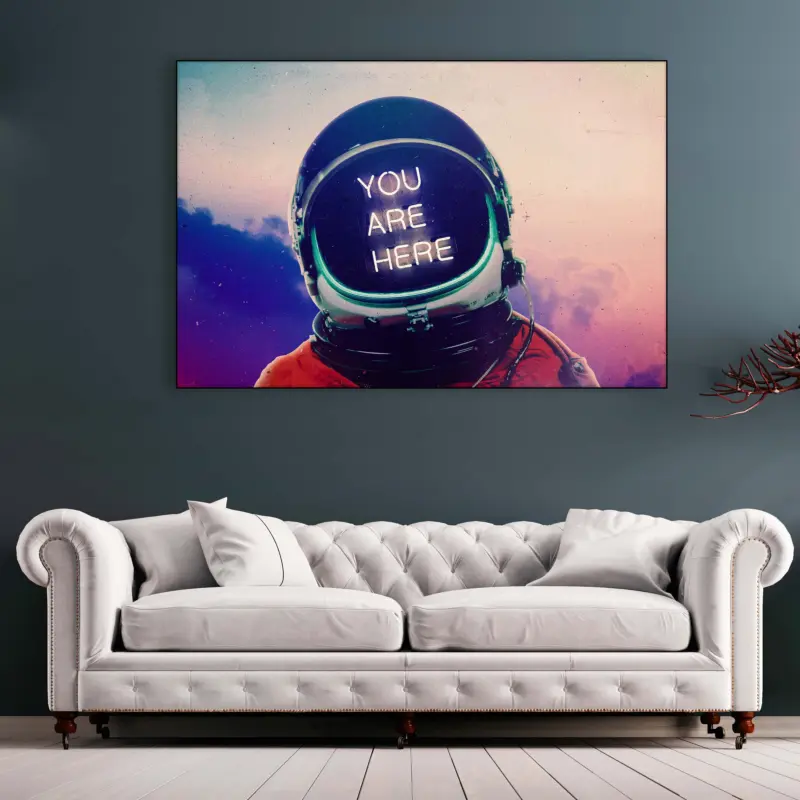 Large horizontal astronaut artwork with "you are here" in neon lettering hangs above neutral couch in living room