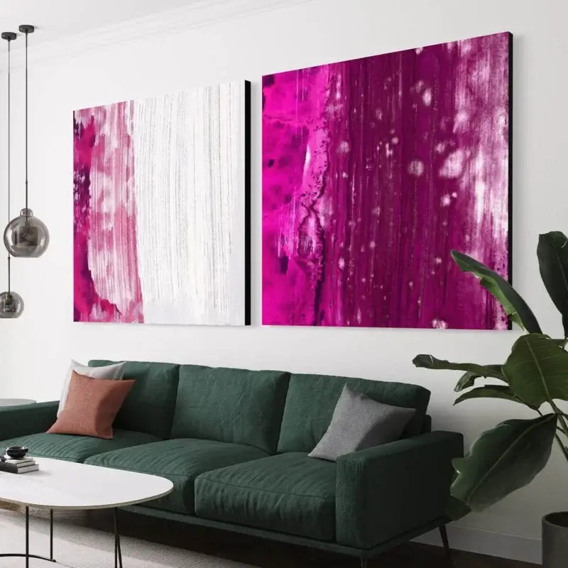 Set of two square abstract paintings in magenta hang side by side in living room above green couch.
