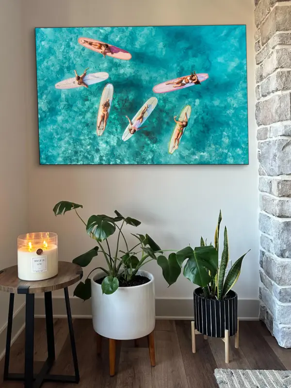 Aerial photo of surfer girls hanging on their boards in Hawaii hangs above indoor house plants and a big ass candle sitting on a side table in a living room