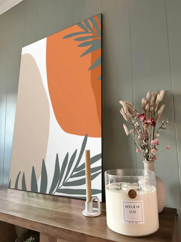 Large orange abstract wall art leans on sage green wall in boho dining room next to sea salt and orchid scented big ass candle and dried floral bouquet.
